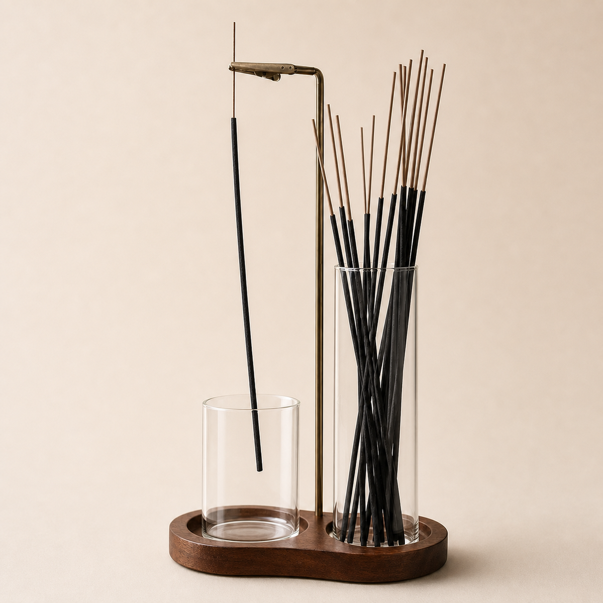 A wooden incense holder set with a brass stand, a glass cup, and a tall glass cylinder filled with black incense sticks, photographed on a warm beige background.