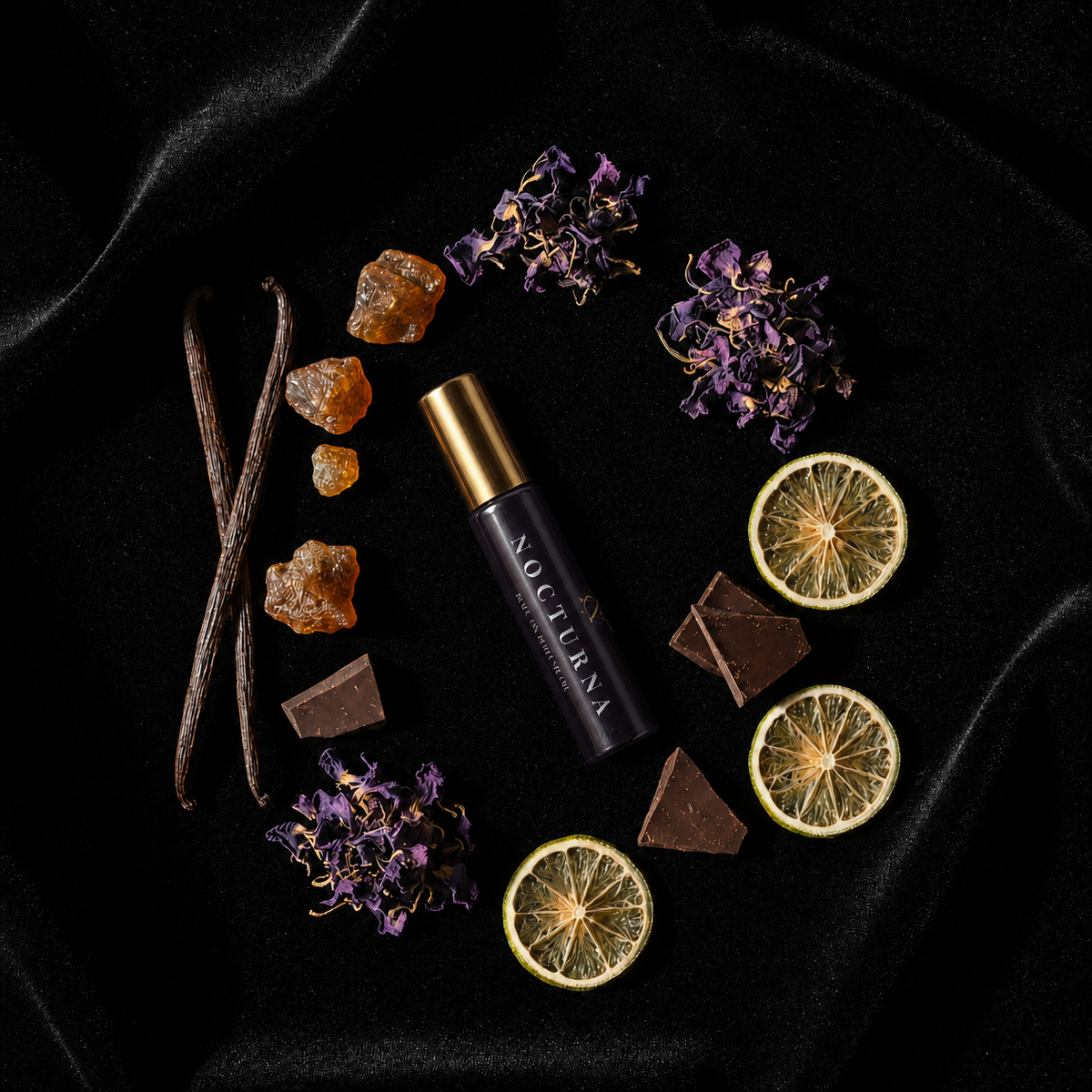 A cosmetic rollerball bottle labeled 'NOCTURNA' lies on a black fabric background, surrounded by styled ingredients including dried purple flowers, vanilla pods, amber crystals, dried lime slices, and dark chocolate pieces.