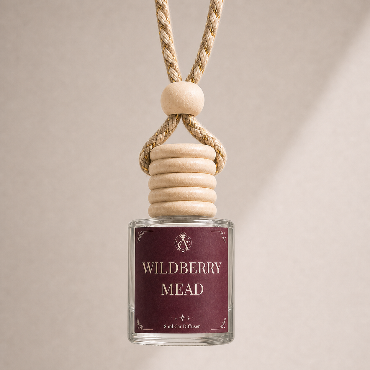 A glass car diffuser bottle with a natural wood cap and a thick woven rope loop, featuring a dark burgundy label that reads 'WILDBERRY MEAD'.